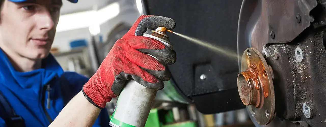 A mechanic sprays fluids from a canister onto a vehicle part.