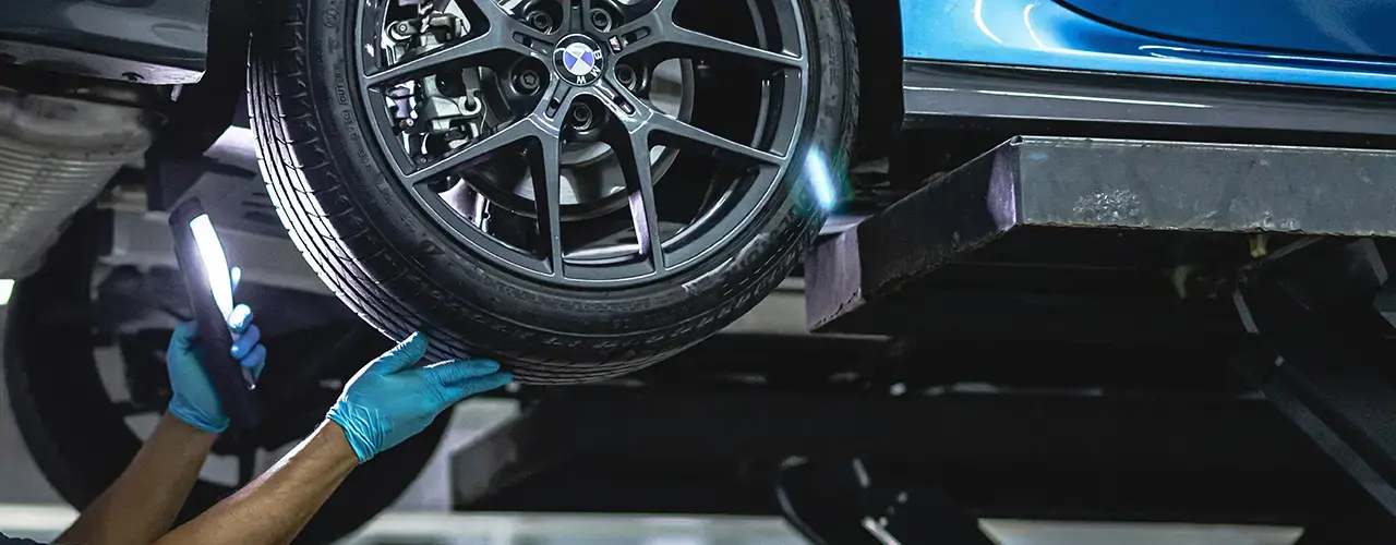 A man inspects a blue car tyre while checking the vehicle for its MOT certification.