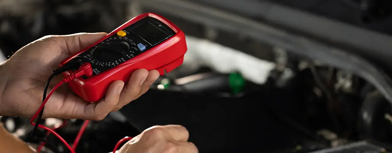 A person holds an electronic multi-meter, checking the voltage of a car battery.