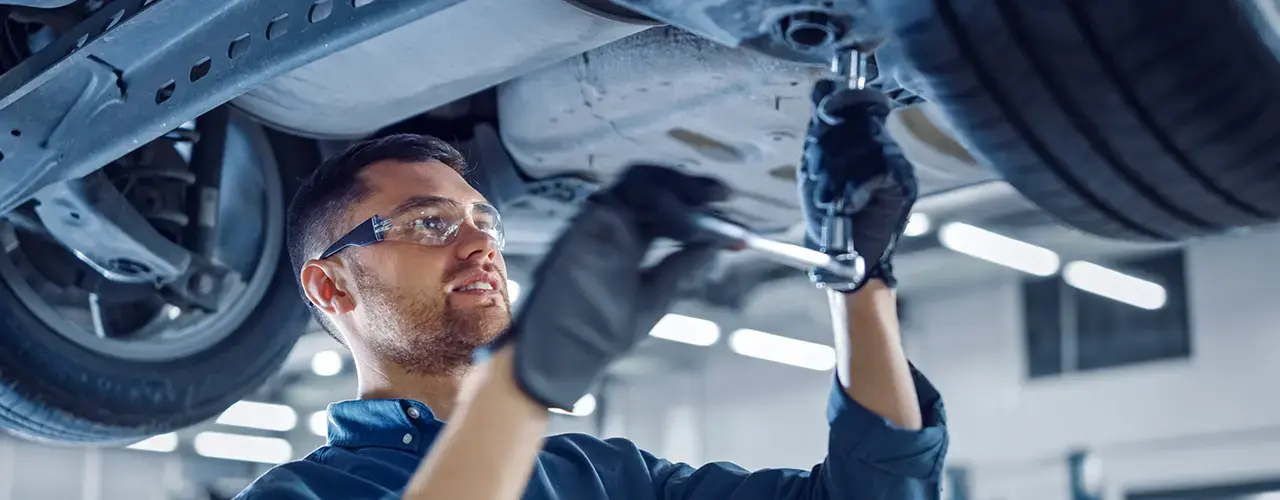 A man wearing glasses is focused on repairing a car in a garage setting.