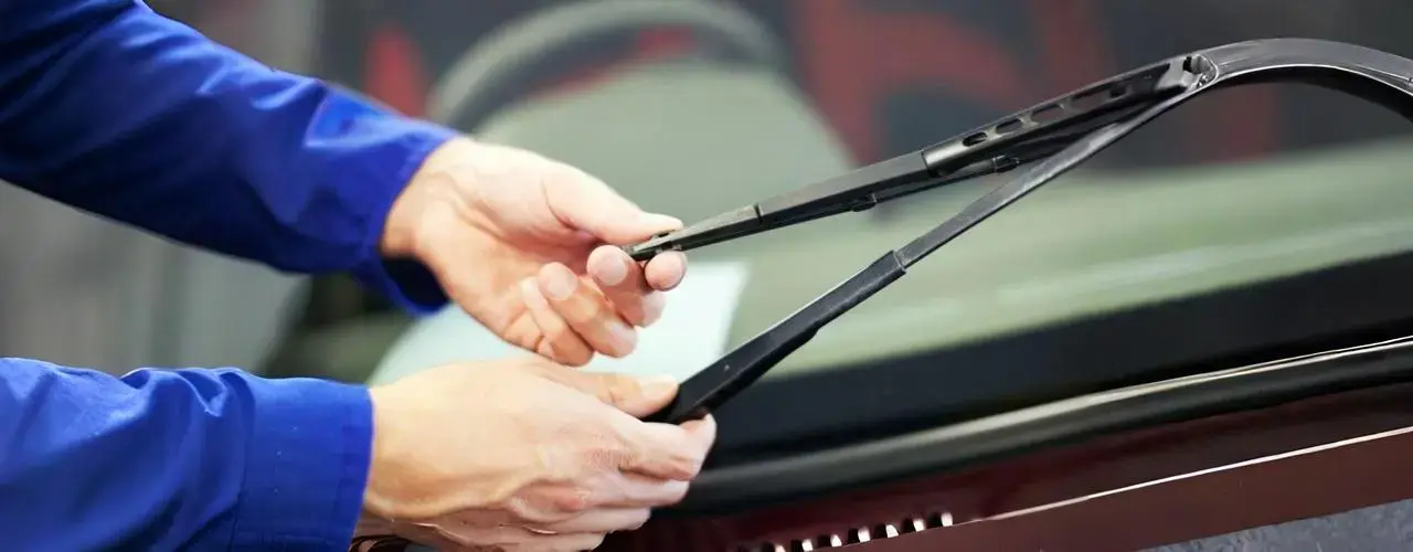 A mechanic trying to remove a windshield wiper blade from a car for replacement.