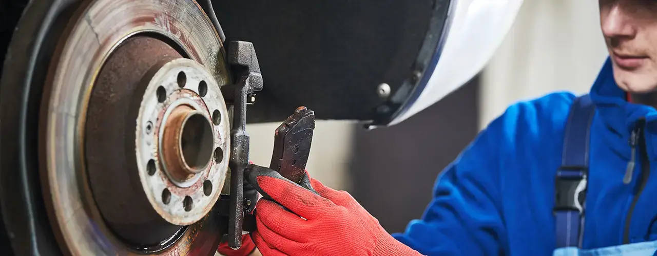 A mechanic in blue overalls repairs a brake.