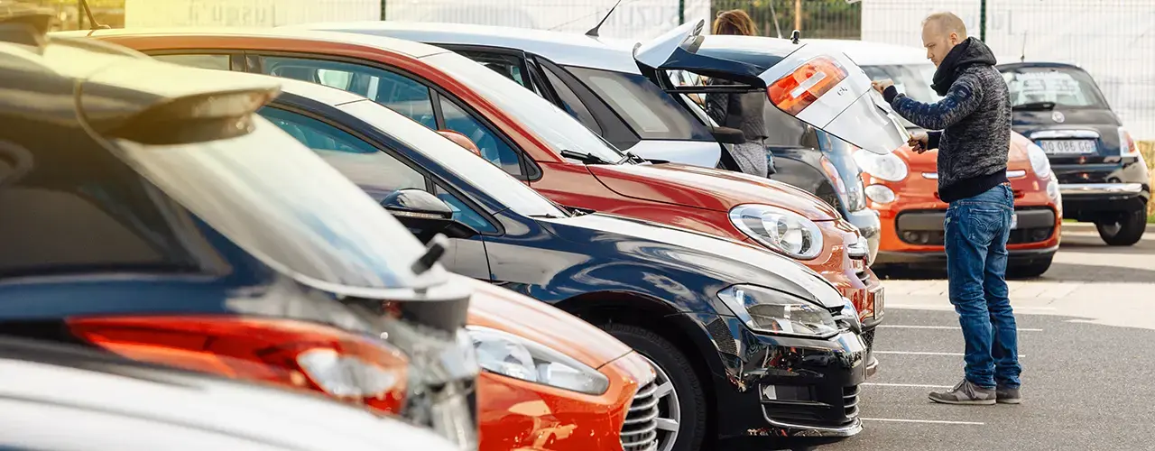 A man standing in a parking lot beside a parked car.