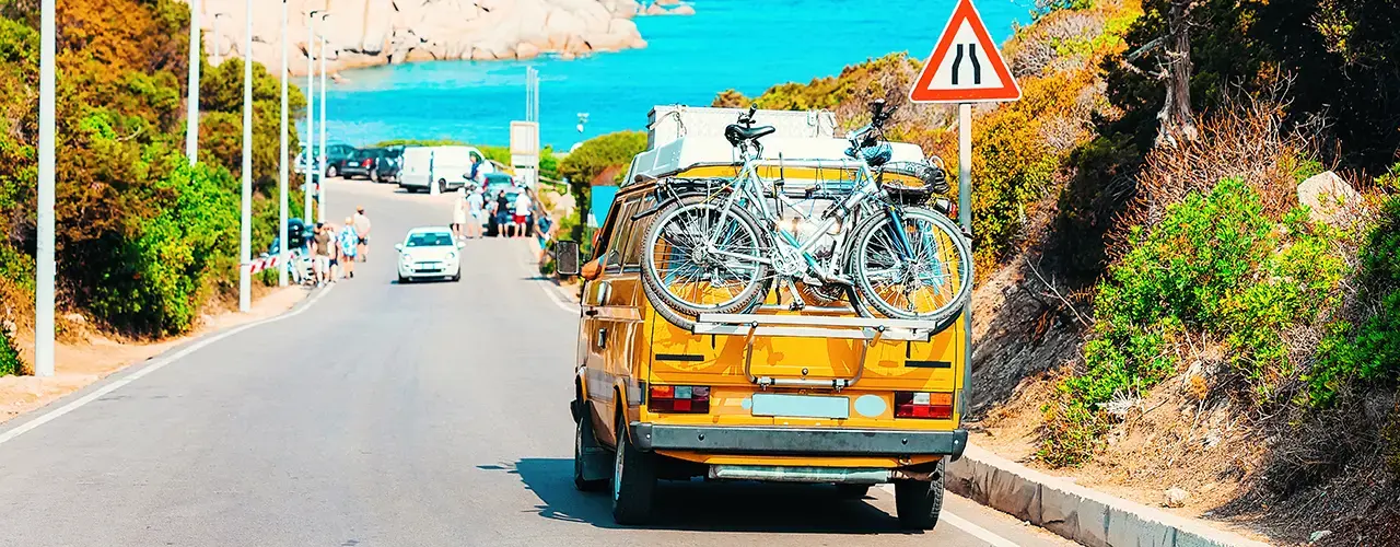 A bright yellow truck with bicycles secured in the back on the open road.